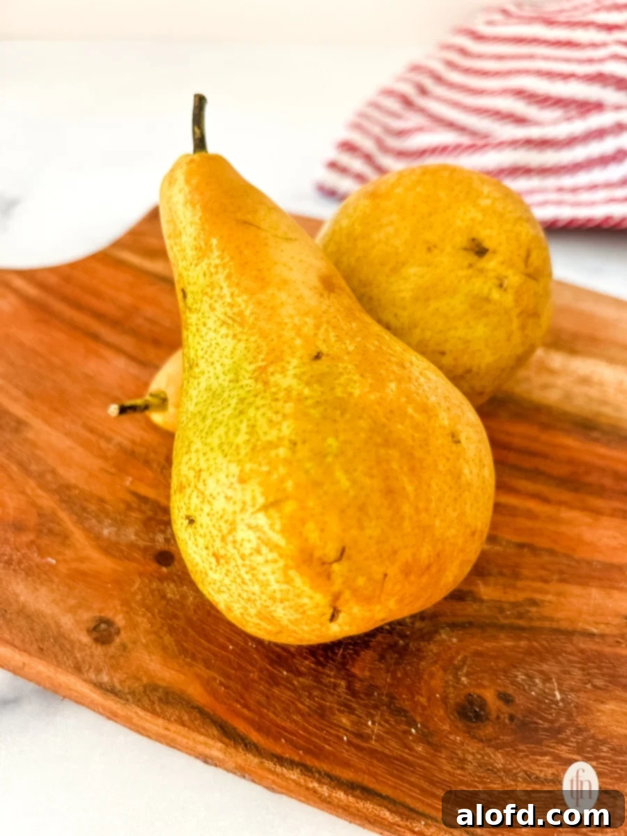 Perfect Pear Slices Every Time 3 Two perfectly ripe pears, one green and one reddish-green, resting on a clean wooden cutting board, ready for preparation.