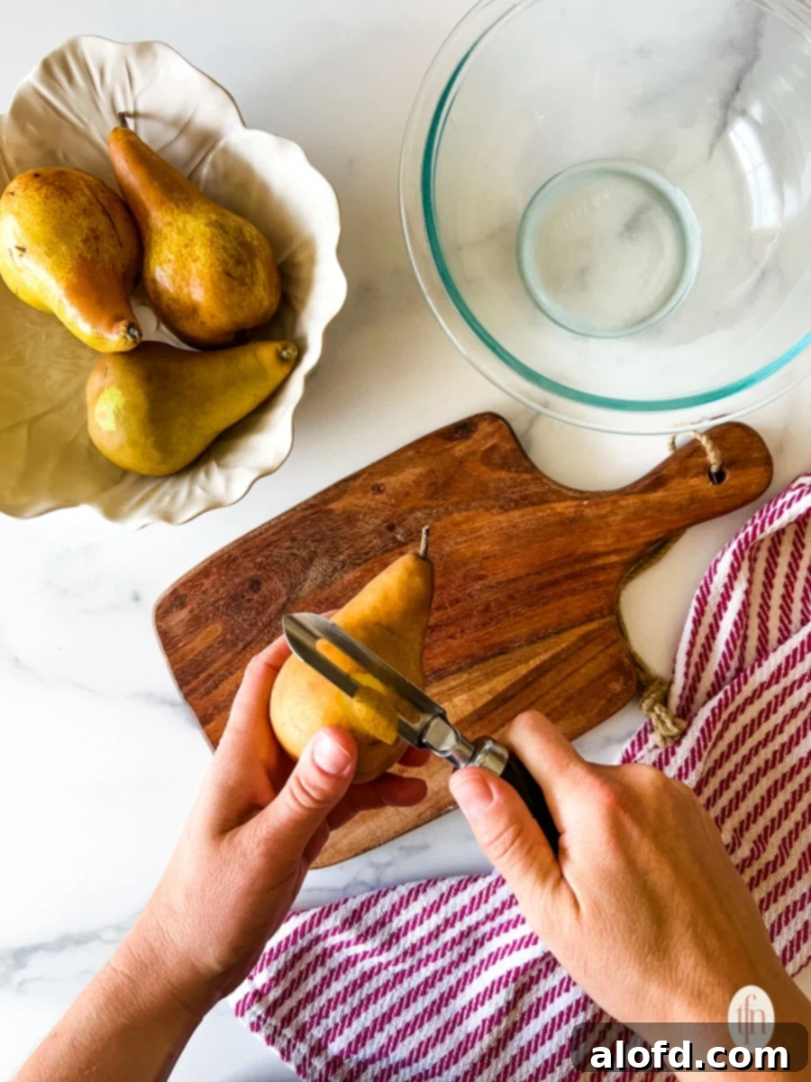 Perfect Pear Slices Every Time 4 A hand expertly peeling a fresh pear with a silver vegetable peeler, revealing the fruit's tender flesh.