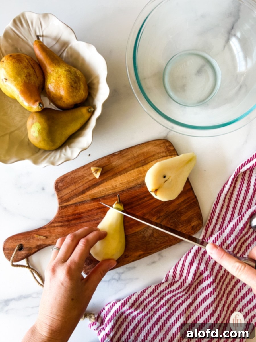 Perfect Pear Slices Every Time 5 A close-up shot of a hand using a sharp knife to slice off the stem end of a fresh pear on a wooden cutting board.