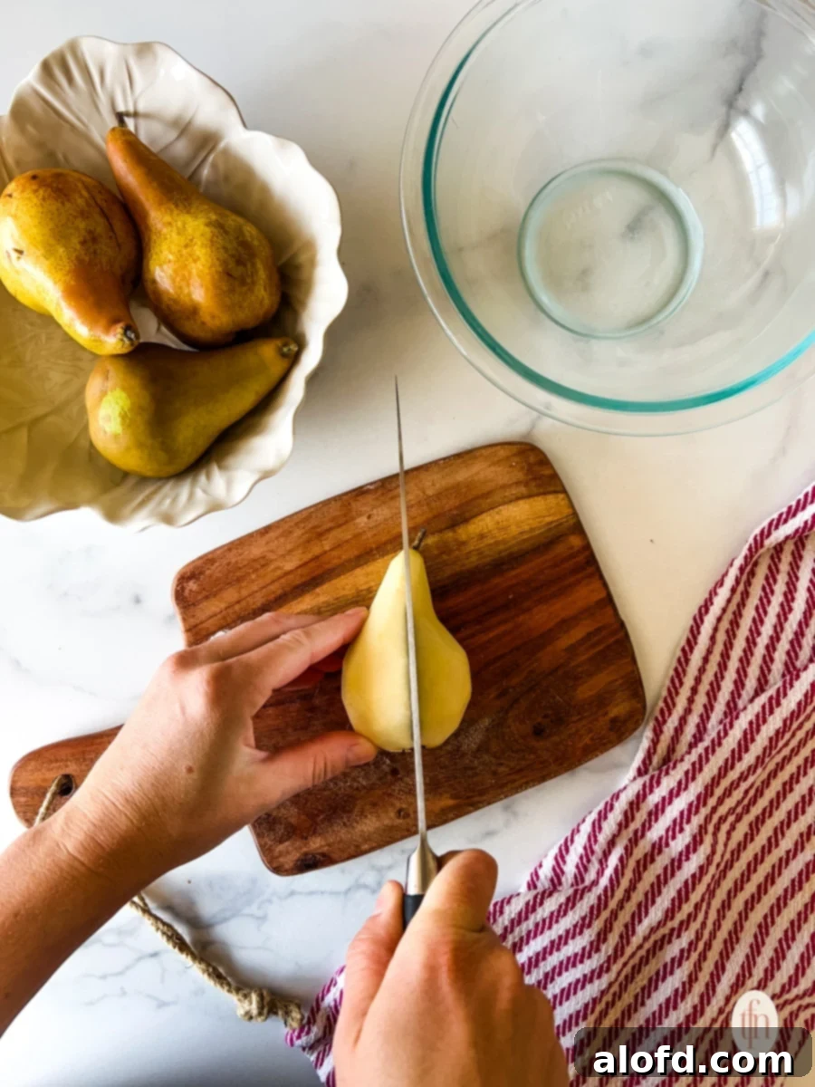 Perfect Pear Slices Every Time 6 A pear being carefully cut in half lengthwise on a wooden cutting board, revealing its core.