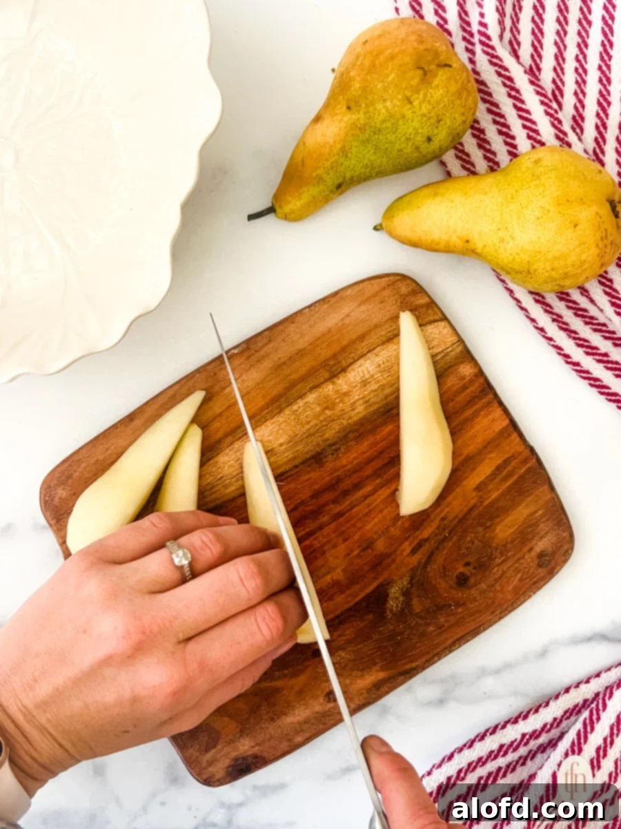 Perfect Pear Slices Every Time 8 A close-up of a hand skillfully slicing a pear half into thin, even pieces on a wooden cutting board, with other slices already prepared.