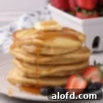 Sourdough Discard Demystified 17 Stacked pancakes with butter and syrup poured on top and fruits on the side.