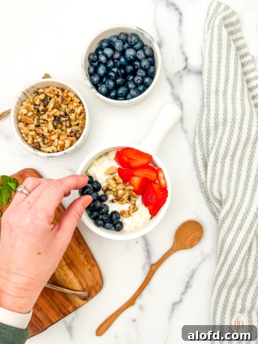 Nourishing Cottage Cheese Creation 8 Assembling the ingredients for cottage cheese and fruit bowls, showing cottage cheese in a bowl topped with strawberries and blueberries.