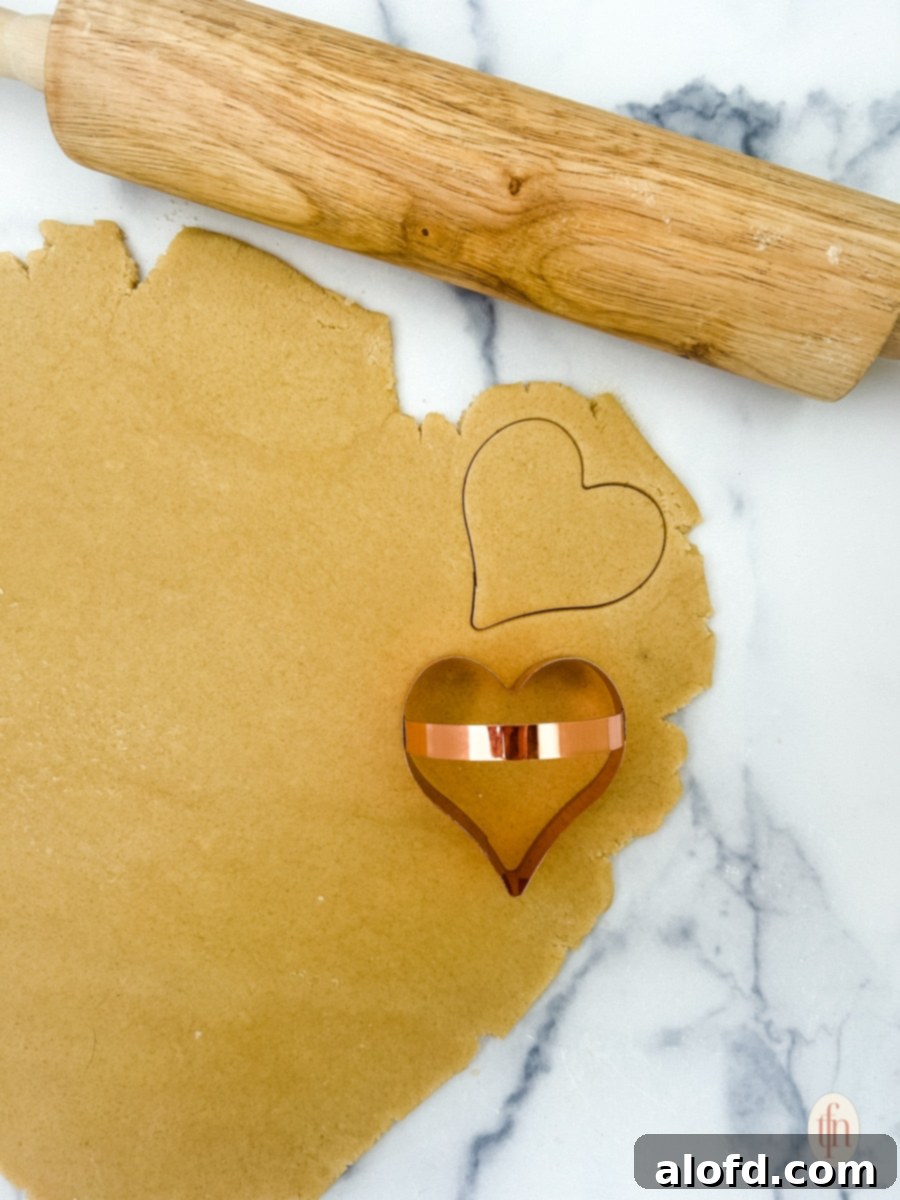 Sweetheart Delights 8 Rolled cookie dough with a rolling pin and a heart cookie cutter, showing the cutting process.