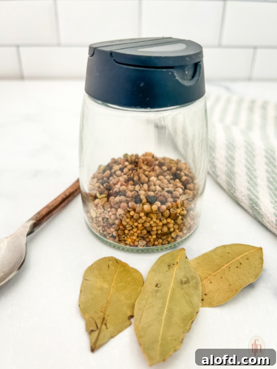 Signature Corned Beef Spice Blend 2 Homemade corned beef seasoning blend in a clear spice jar, accompanied by whole bay leaves and a small spoon, ready for use.