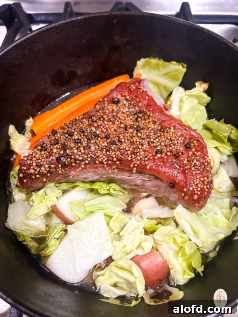 Slow-Braised Dutch Oven Corned Beef 8 Beef with seasoning on top and vegetables in a Dutch oven.