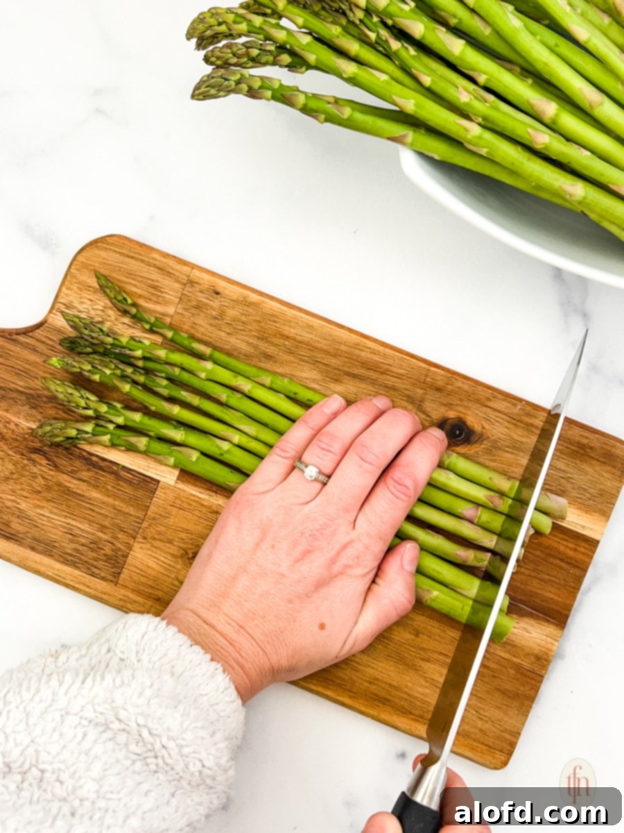 Creamy Asparagus Cheese Bake 6 A chef's knife trimming the woody ends of fresh asparagus spears on a wooden chopping board.