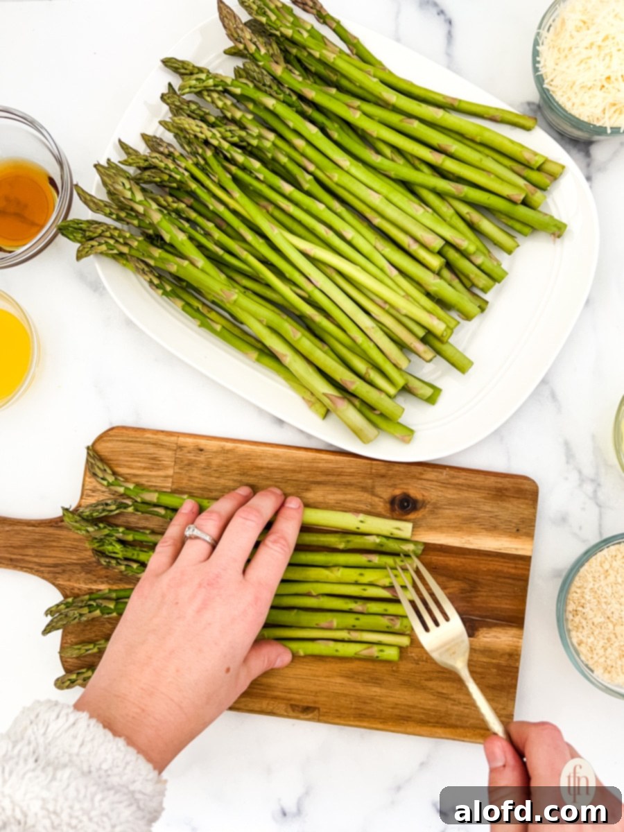 Creamy Asparagus Cheese Bake 7 A fork poking holes into asparagus spears laid on a wooden chopping board, with other ingredients nearby.