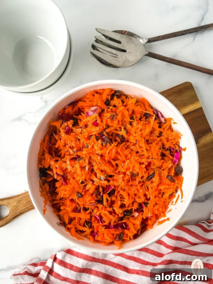 Vibrantly shredded carrots and raisins in a white bowl, ready to be dressed.