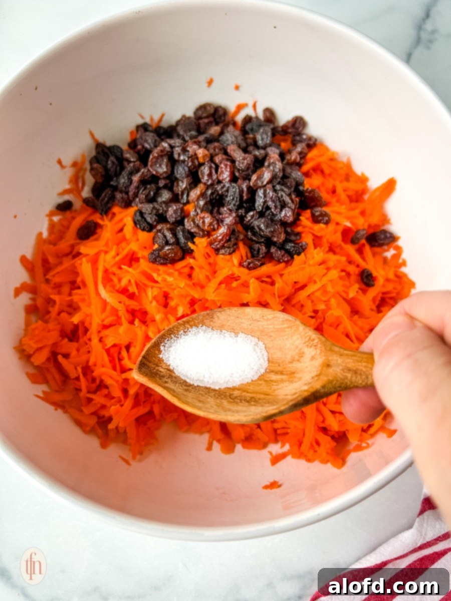 Shredded carrots and raisins being added to a mixing bowl.