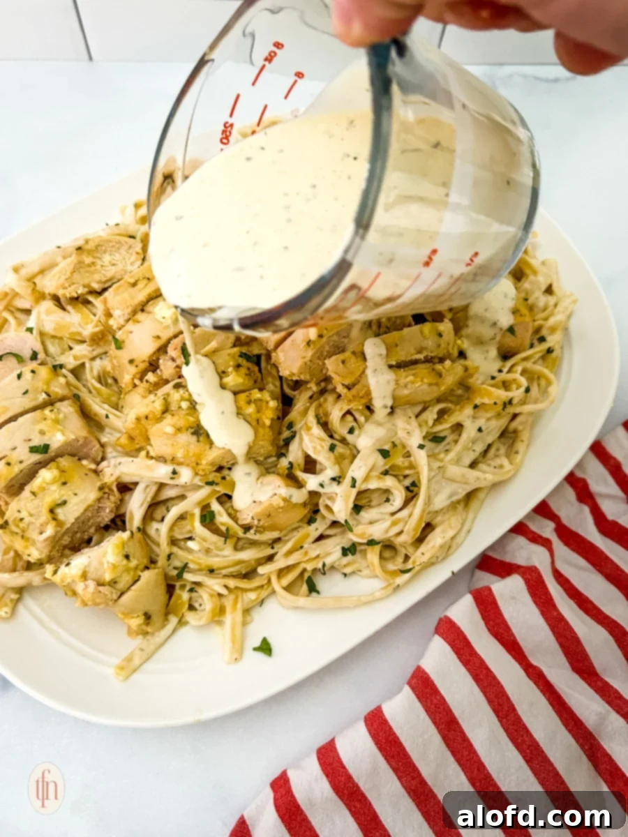 Creamy Garlic Parmesan Chicken Pasta 7 Pouring creamy garlic parmesan sauce over a serving of chicken and fettuccine pasta.