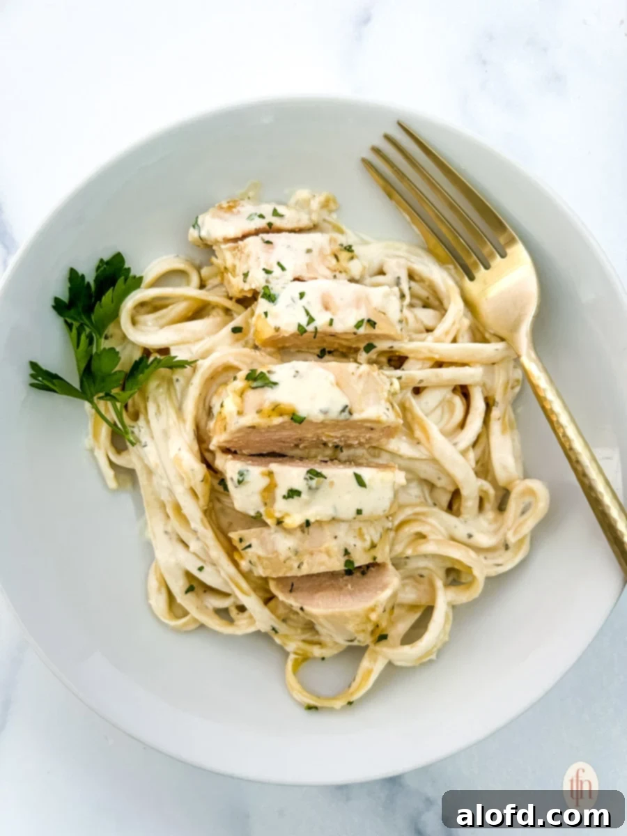 Creamy Garlic Parmesan Chicken Pasta 8 A close-up shot of creamy garlic parmesan chicken pasta garnished with fresh herbs in a white bowl.
