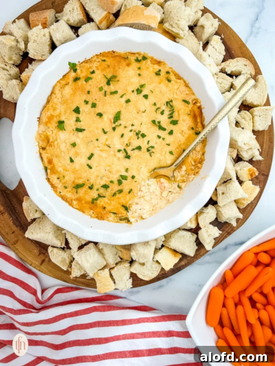 A bowl of Cajun crab dip with shrimp and croutons served on a rustic wooden platter with a side of carrots.