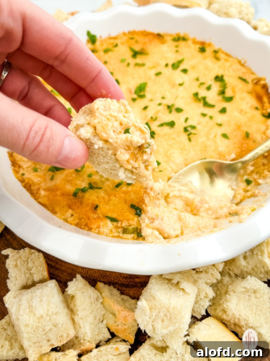 Croutons being dipped into a bowl of bubbly Cajun crab dip with shrimp.