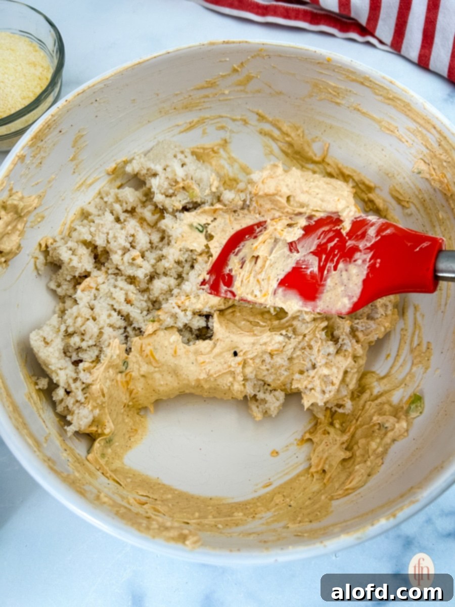 Gently mixing seafood into the creamy dip base with a rubber spatula for Cajun crab dip.