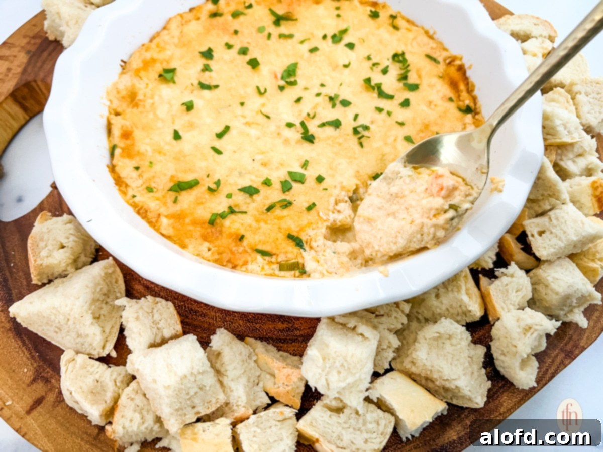 A bowl of Cajun crab dip with shrimp and croutons served on a wooden platter, ready for dipping.