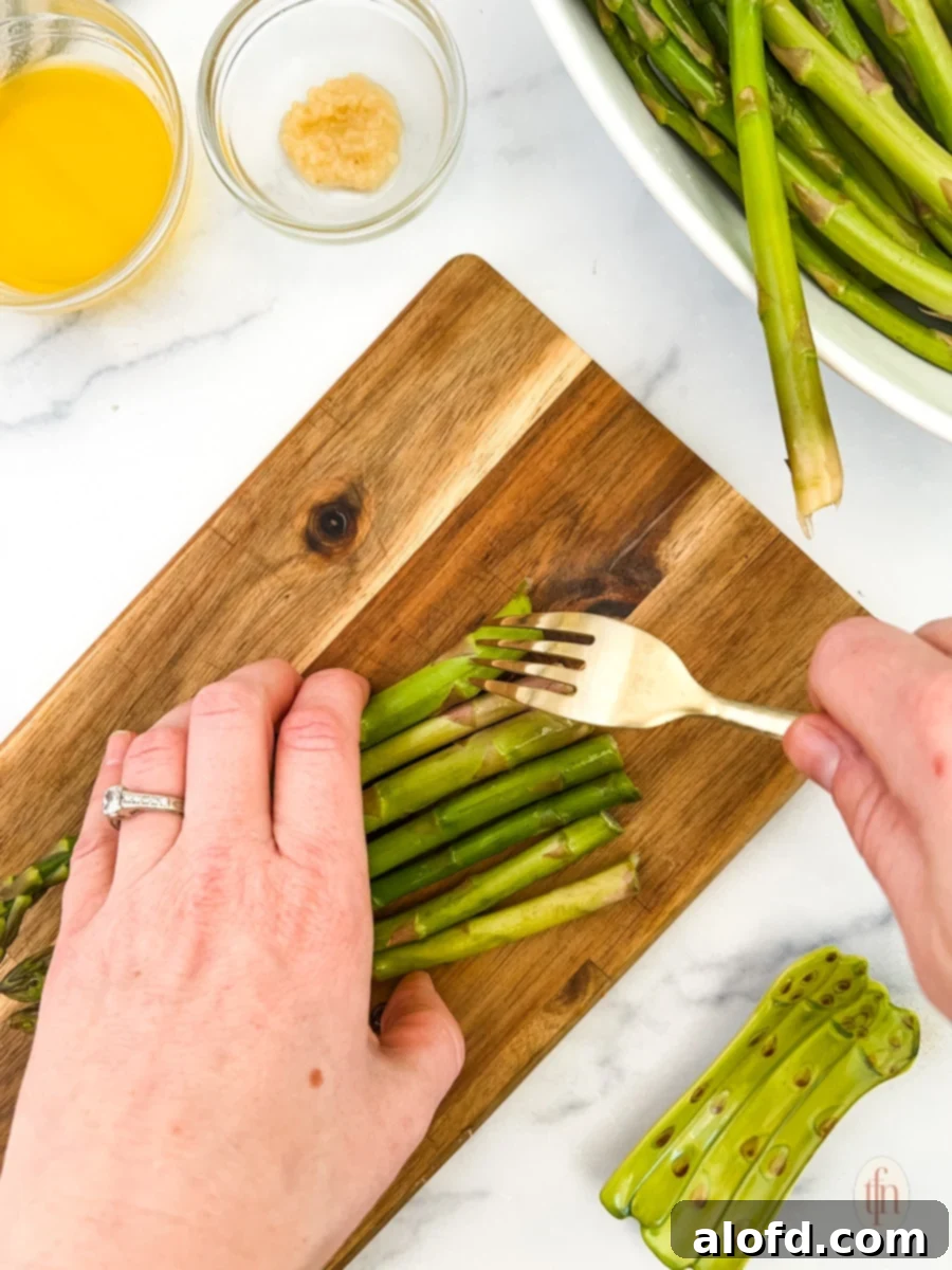 Golden Roasted Carrots and Asparagus 5 A fork gently poking holes into asparagus spears on a wooden cutting board, a crucial step for tenderizing them before roasting.