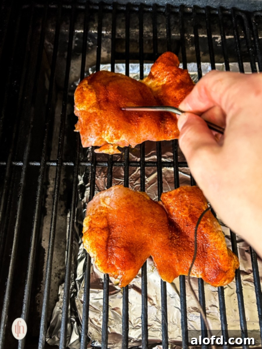 Checking the smoked chicken thigh's temperature using a Meater while on the griller.