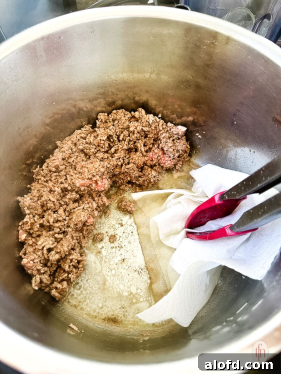 Tongs holding a paper towel to absorb the fat rendered from the sautéed ground beef.