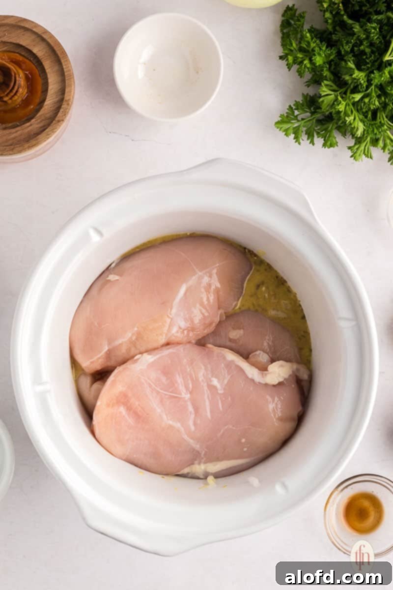 Sweet and Tangy Slow Cooker Honey Mustard Chicken 7 adding breasts to the honey garlic sauce in the crockpot.