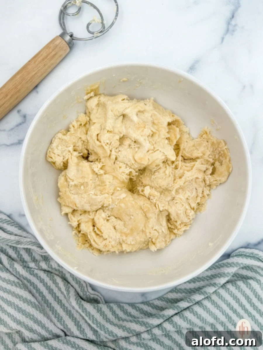 Artisan Sourdough Flatbread 5 Sourdough dough mixture in a white bowl with a dough whisk on the table, after initial mixing.