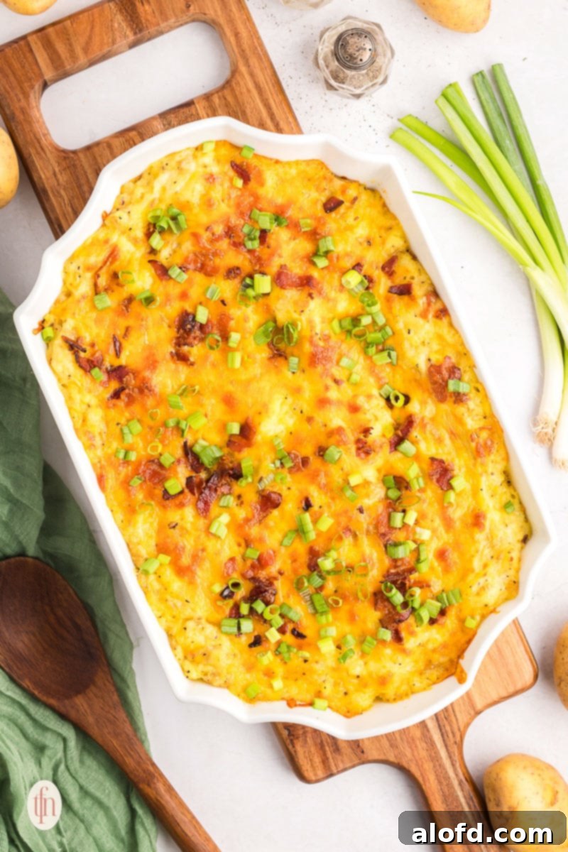 A large casserole dish of golden-brown twice baked mashed potatoes, garnished with green onions and bacon, served on a rustic wooden board.