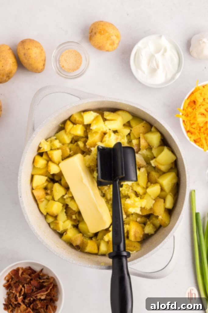 Hot boiled potatoes and melted butter in a cooking pot, ready for mashing.