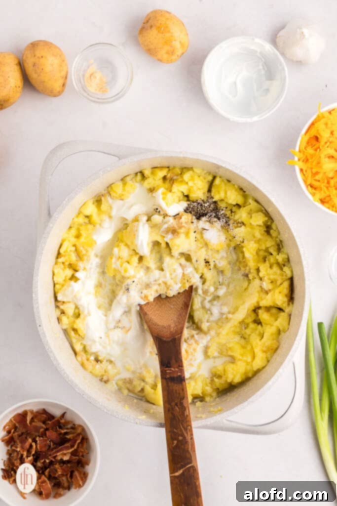 Mashed potatoes being mixed with warm milk and cream in a pot, creating a smooth consistency.