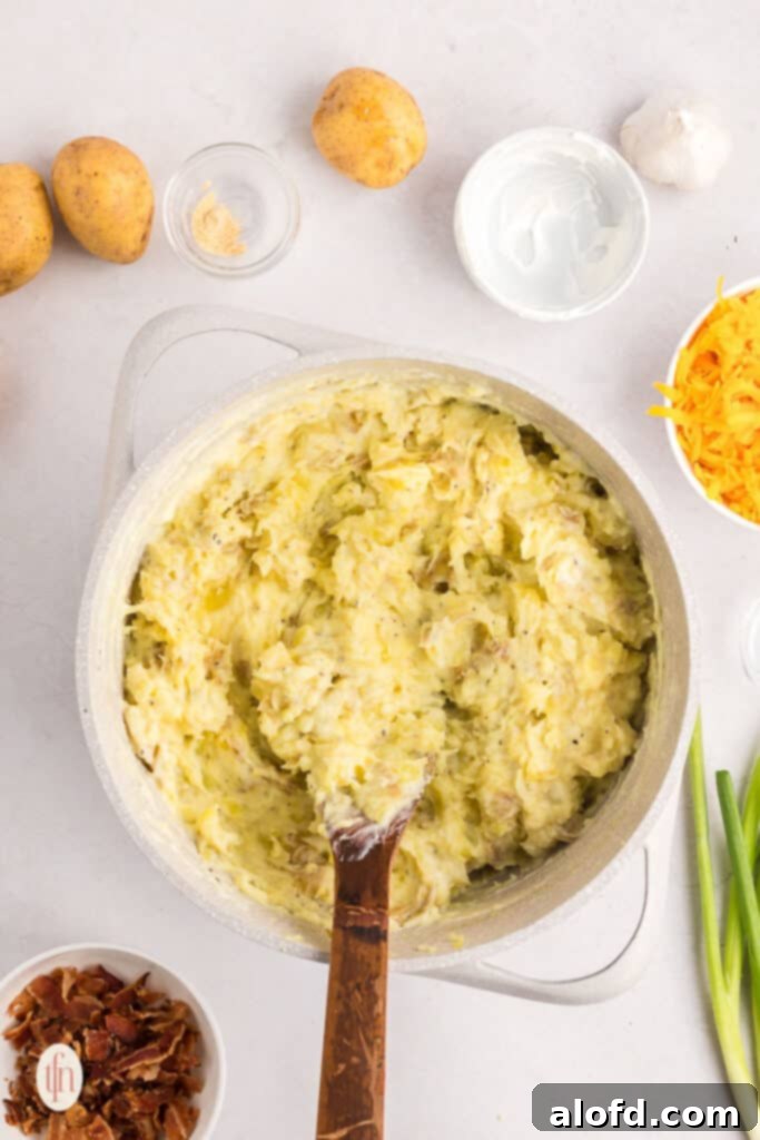 A smooth, creamy mixture of seasoned mashed potatoes in a pot with a wooden spoon.