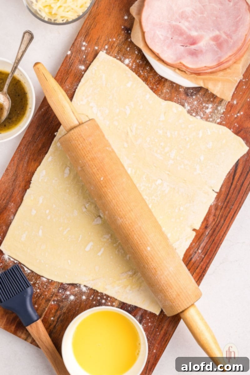 A rolling pin shown resting on a sheet of puff pastry, indicating the start of the preparation process.