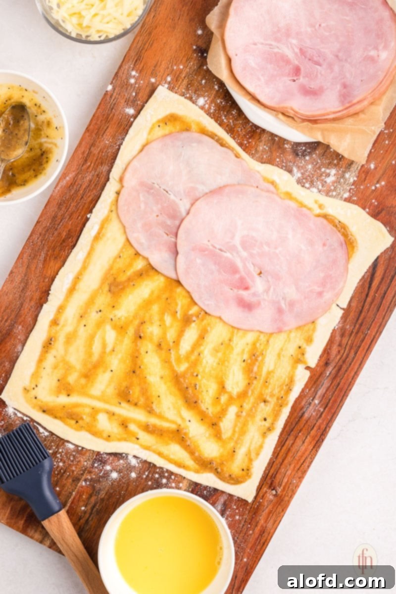 Puff pastry spread with sauce and layered with ham on a wooden board, ready for the next step.