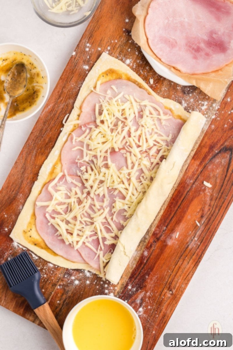 Puff pastry being carefully rolled up into a log on a wooden board, forming the pinwheel shape.