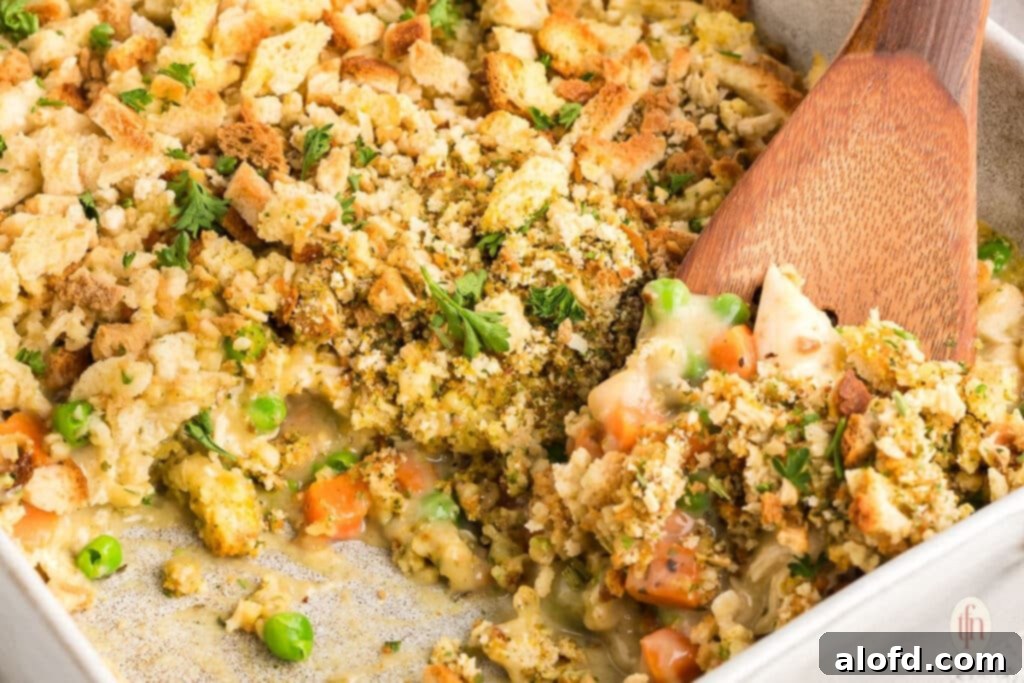 A large serving of chicken stuffing casserole in a baking dish, with a wooden spoon ready to dish it out.
