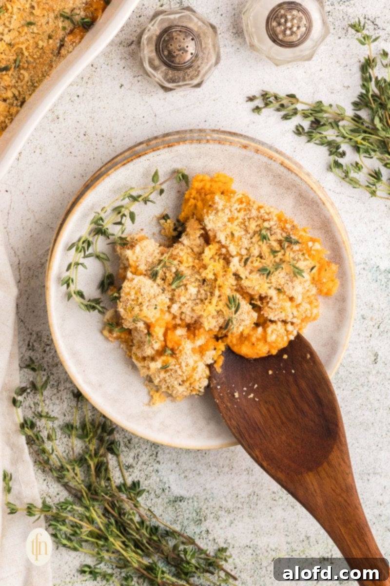 A scoop of savory sweet potato casserole on a plate with wooden spoon and fresh herbs.