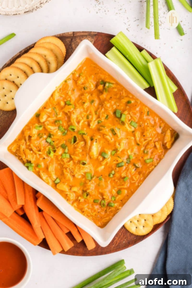 Creamy Dairy-Free Buffalo Chicken Dip 2 A vibrant, warm dairy-free buffalo chicken dip served in a rustic bowl, surrounded by a colorful assortment of dippers like crisp celery sticks, carrot sticks, and toasted pita bread on a wooden platter.