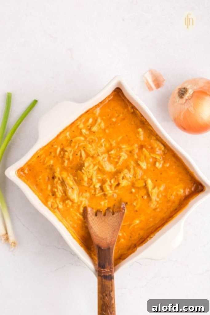 Creamy Dairy-Free Buffalo Chicken Dip 11 Hot, bubbly dairy-free buffalo chicken dip in a white baking dish, freshly removed from the oven and stirred, ready for its final resting period to thicken.