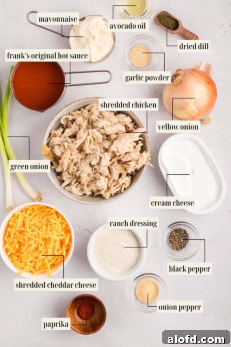 Creamy Dairy-Free Buffalo Chicken Dip 5 A flat lay image displaying all the essential ingredients for making dairy-free buffalo chicken dip, clearly labeled and arranged on a rustic wooden surface, including shredded chicken, dairy-free cream cheese, hot sauce, and seasonings.