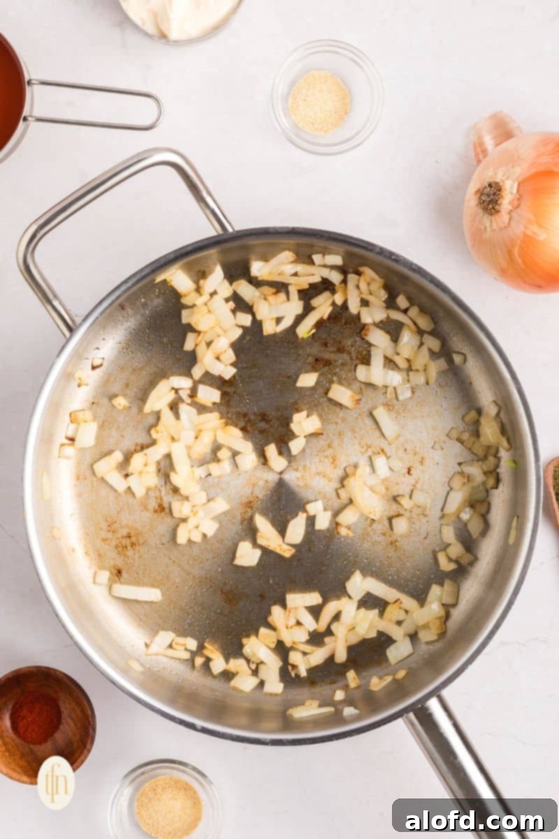 Creamy Dairy-Free Buffalo Chicken Dip 7 Finely chopped yellow onions gently sautéing in a hot skillet with avocado oil, becoming translucent and fragrant, ready for the next step of the dairy-free buffalo chicken dip preparation.