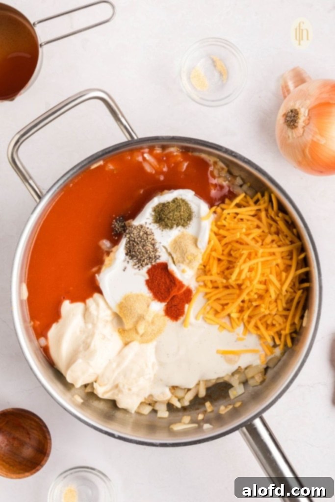 Creamy Dairy-Free Buffalo Chicken Dip 8 Close-up of dairy-free cream cheese, shredded cheddar, and hot sauce being stirred together in a skillet, creating a creamy, vibrant orange base for the buffalo chicken dip.