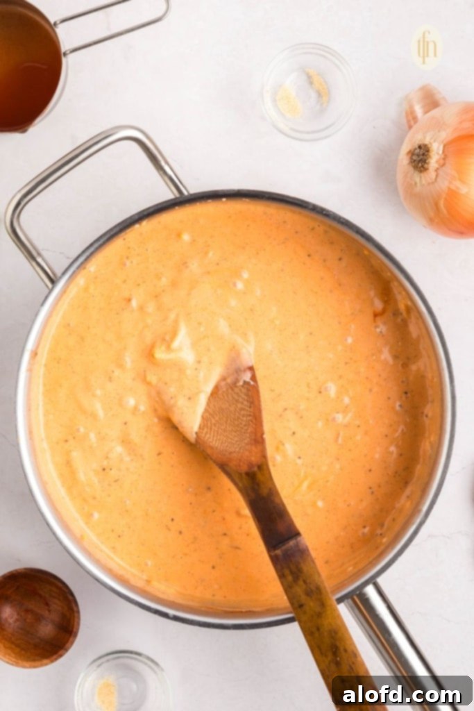 Creamy Dairy-Free Buffalo Chicken Dip 9 The creamy, orange buffalo sauce base for the dairy-free chicken dip, thoroughly mixed and smooth in a skillet, with a wooden spoon resting in it.