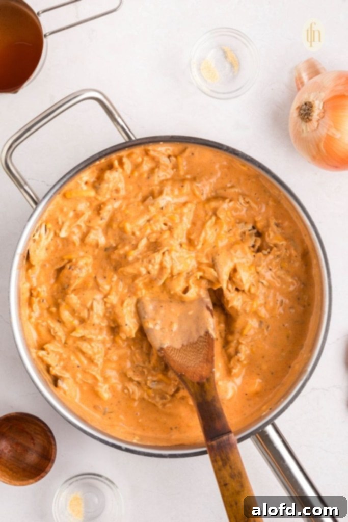 Creamy Dairy-Free Buffalo Chicken Dip 10 Shredded chicken being stirred into the rich, creamy buffalo sauce in a skillet, ensuring every piece is well-coated for a flavorful dairy-free dip.