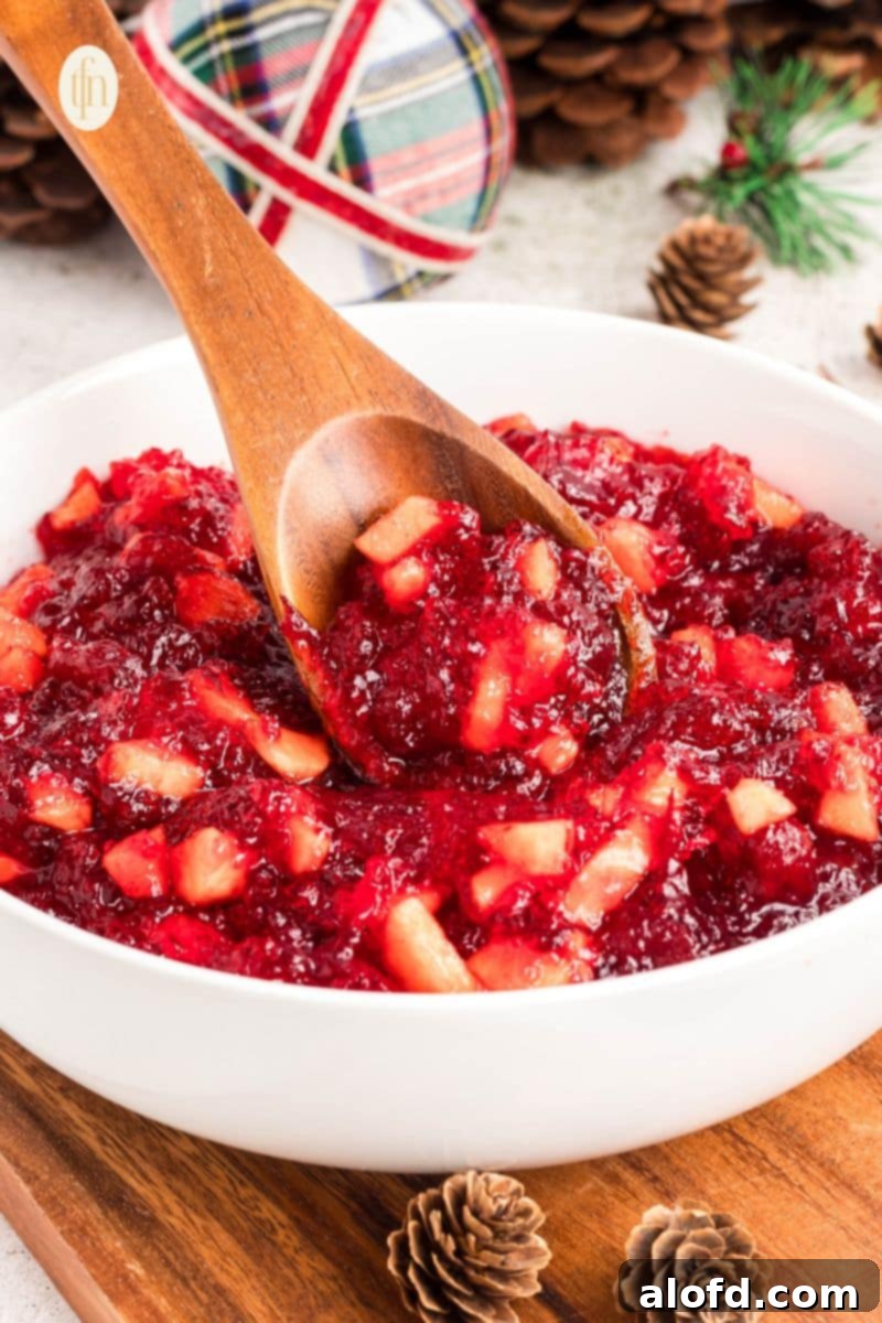 A vibrant red Jello mixture in a white bowl, ready for chilling, with a wooden spoon beside it.
