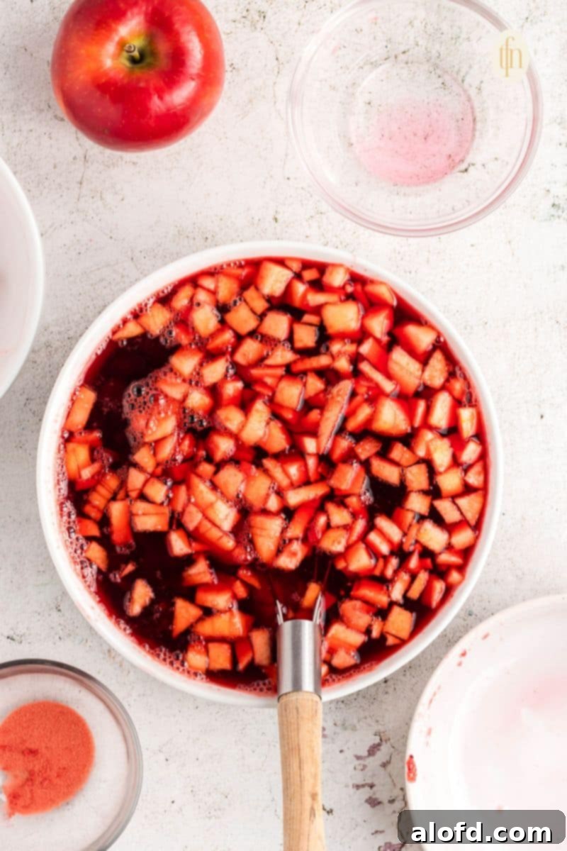 A bowl of fruit with red liquid, showing the cranberry jello salad fully mixed before chilling.