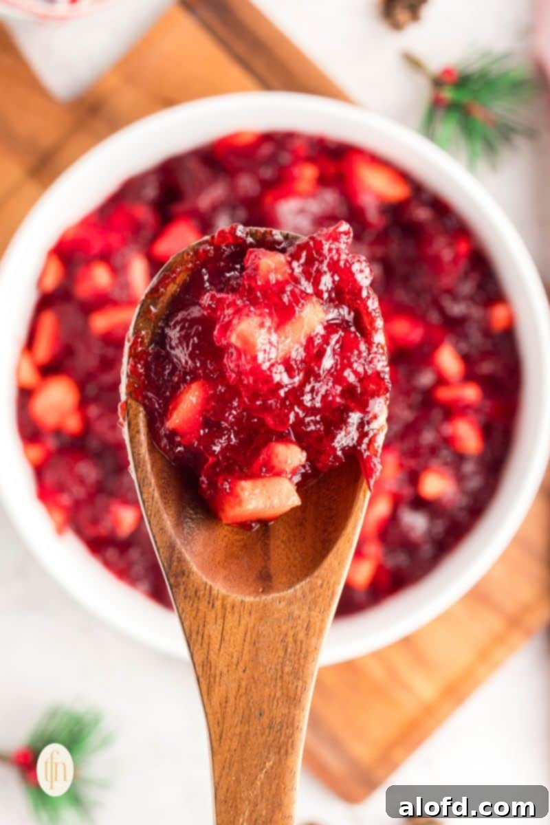 A scoop of the cranberry jello salad in a white bowl with a wooden spoon, garnished with a few fresh cranberries and mint leaves.