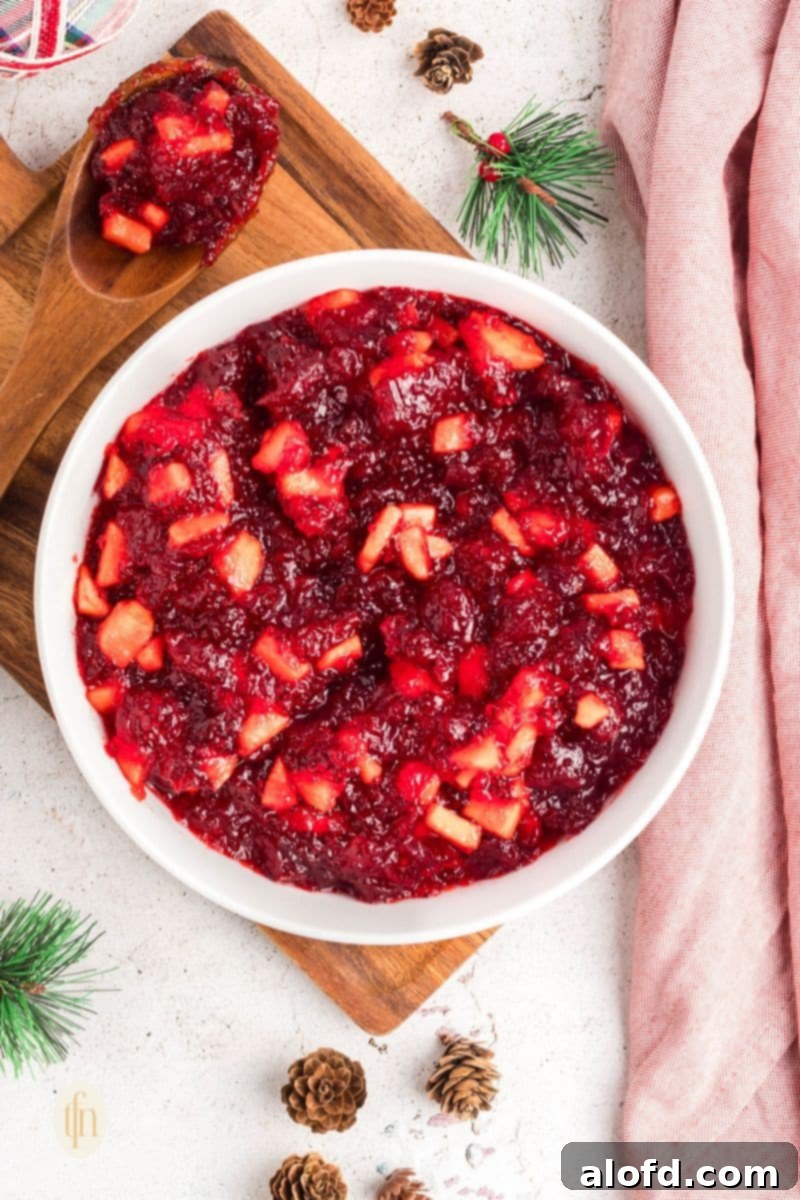 A bowl of red jello mixture with fruit, placed on a rustic wooden board, ready for chilling.