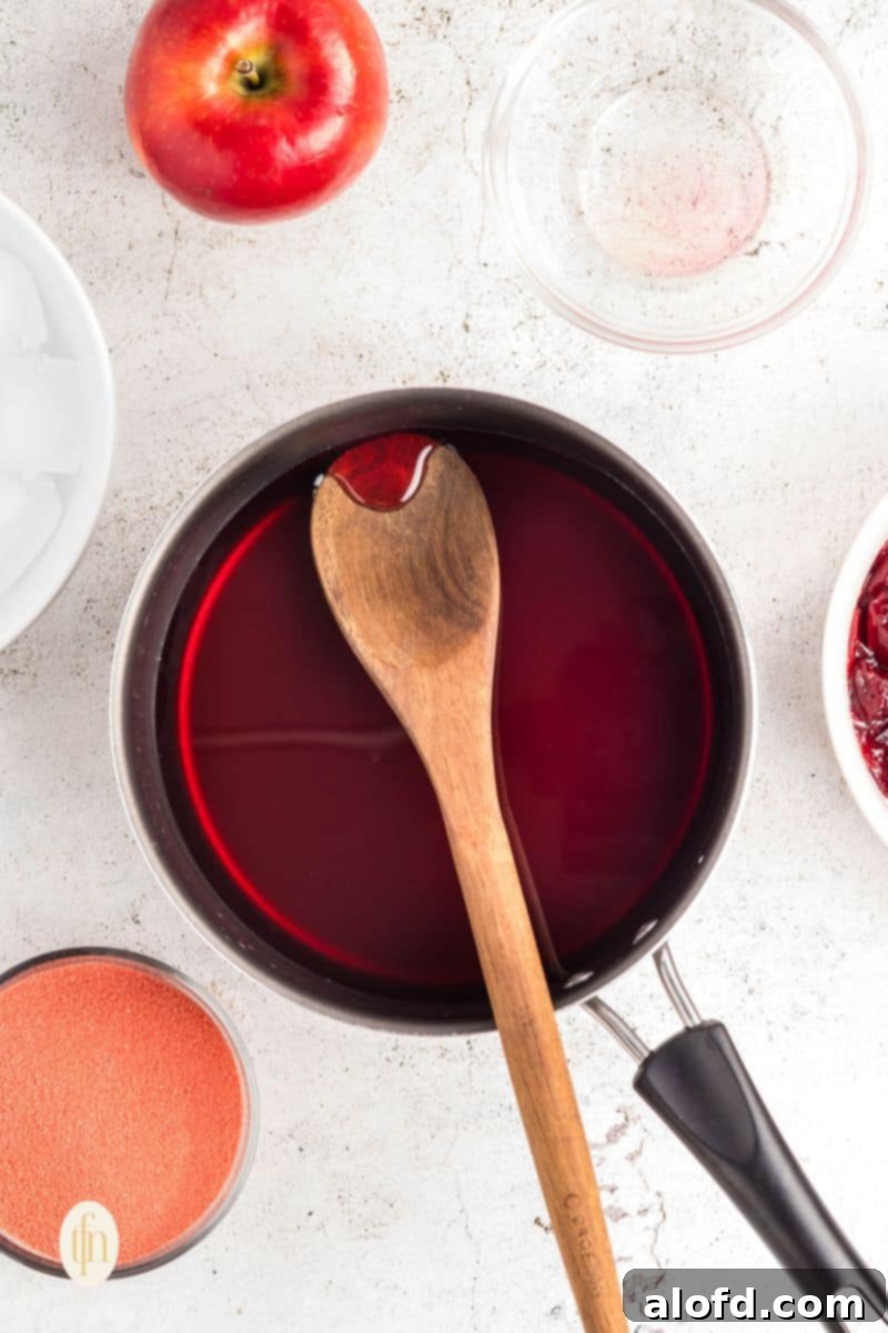 A saucepan with red liquid, likely cranberry juice, with a wooden spoon, indicating the first step of heating.