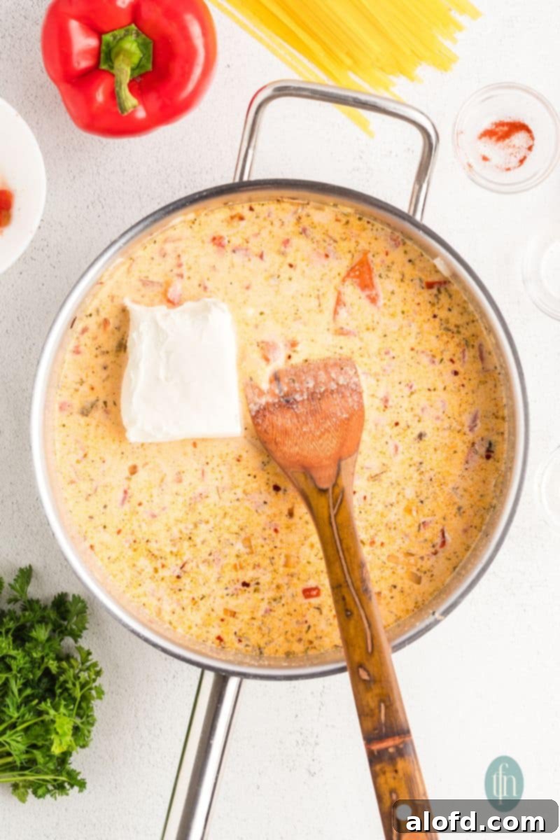 Spicy Rotel Chicken Spaghetti Casserole 11 A block of cream cheese melting into the simmering sauce in a pan.