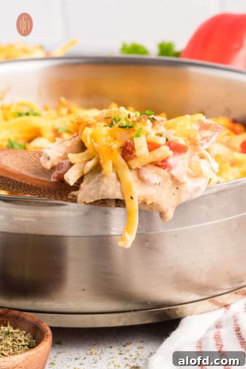 Spicy Rotel Chicken Spaghetti Casserole 17 A wooden spoon scooping a generous portion of cheesy Rotel chicken spaghetti from a pan, showing off its creamy texture.