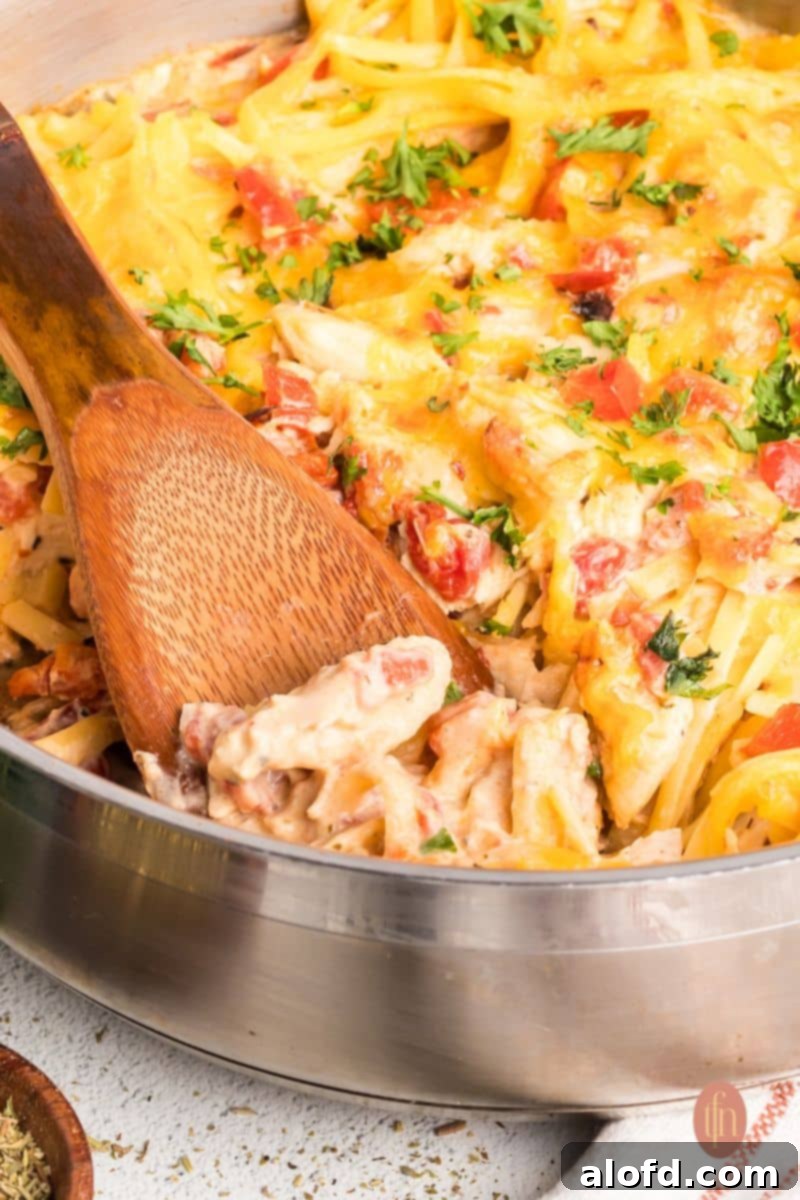Spicy Rotel Chicken Spaghetti Casserole 4 A close-up of cheesy Rotel chicken spaghetti in a large pan, with a wooden spoon scooping out a portion.