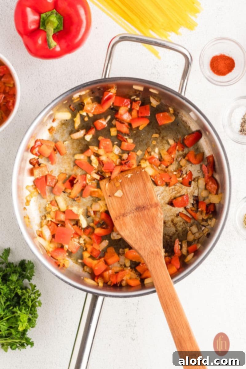 Spicy Rotel Chicken Spaghetti Casserole 7 Sautéed bell peppers and onions in a skillet with a wooden spoon.